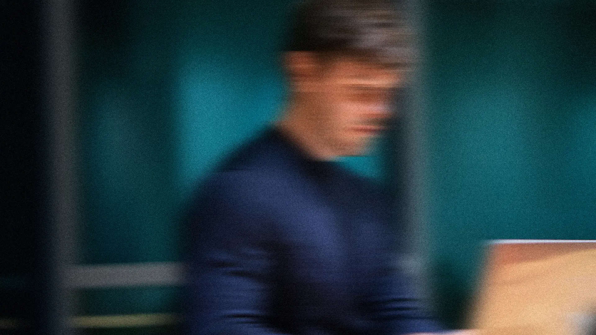 A man working at a laptop in a teal-lit office